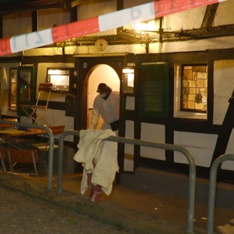 Ein Polizeiflatterband sperrt eine Gaststätte in Rösrath-Hoffnungsthal am Abend des 17. März 2025 ab. Ein Ermittler der Polizei steht in der Tür.