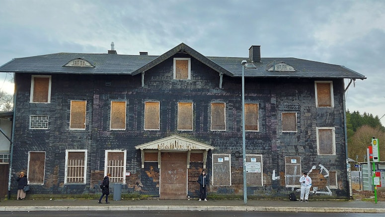 Das Bild zeigt das ehemalige Bahnhofsgebäude. Die Fenster und Türen sind mit Holzplatten zugenagelt.