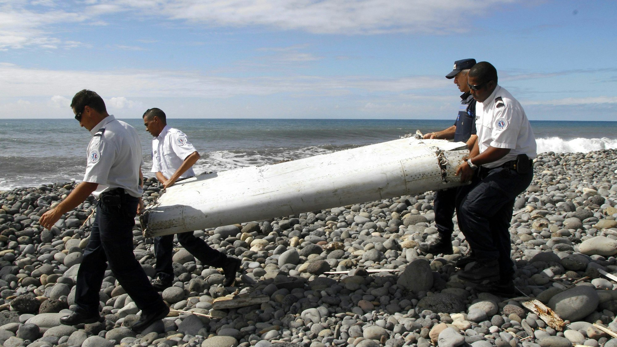 Techniker tragen ein Wrackteil, die Flügelklappe eines Flugzeugs, über einen Strand bei Saint-Andre de la Reunion. Die Suche nach dem Wrack des vor elfeinhalb Jahren verschollenen Fluges MH370 der Malaysia Airlines wird noch in diesem Jahr fortgesetzt.