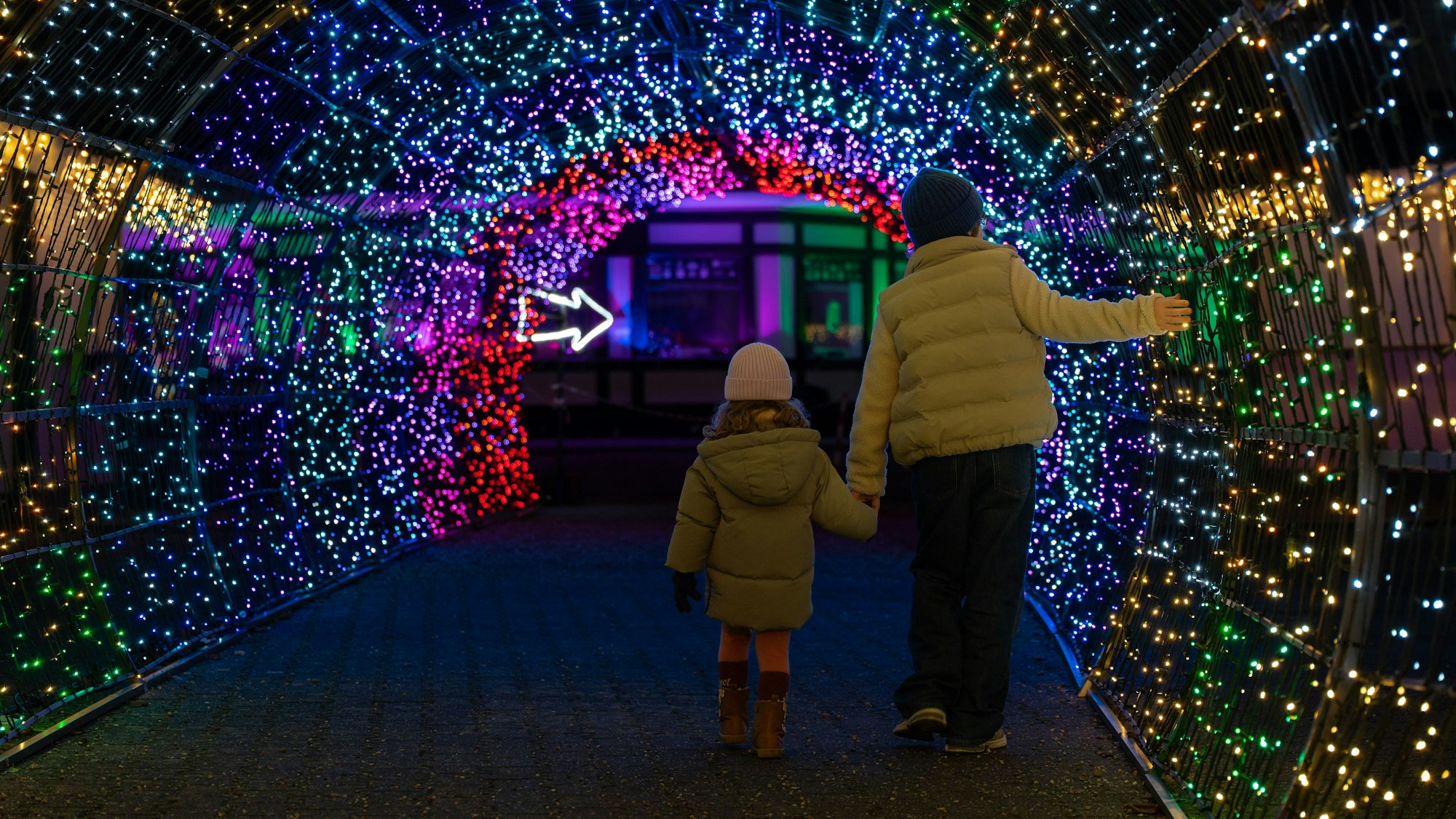 Zwei Kinder gehen durch einen Tunnel mit funkelnden Lichtern bei Garden of Lights in Köln.