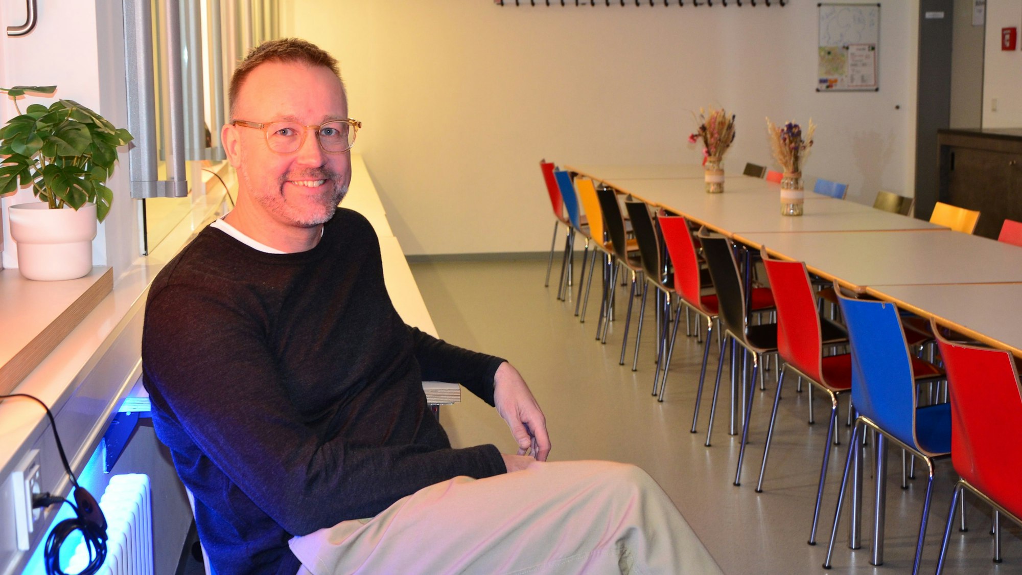 Ein Mann sitzt in einem Raum mit einem langen Tisch und Stühlen.