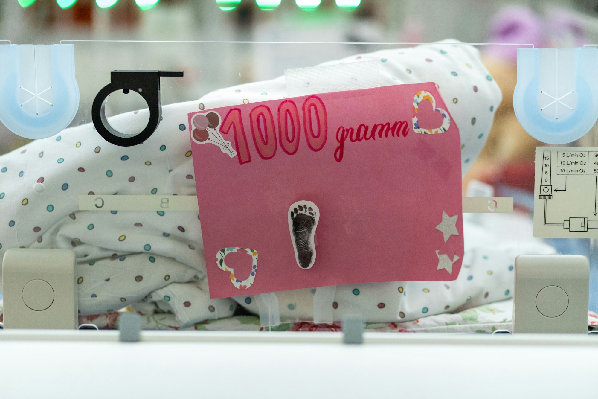 Ein pinkes Schild mit einem kleinen Fußabdruckt drauf und der Aufschrift „1000 Gramm“ hängt am Fußende eines Wärmebetts.