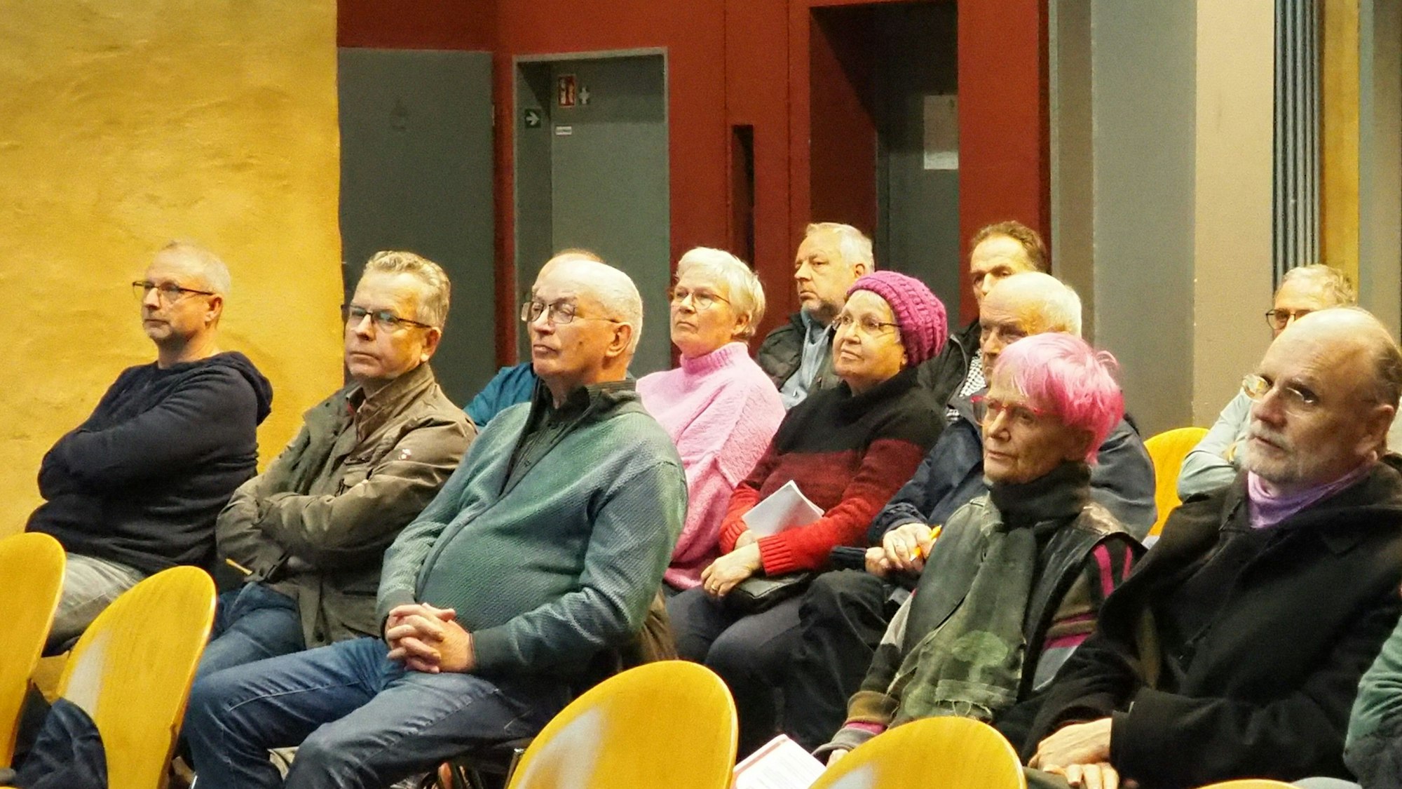 In mehreren Stuhlreihen sitzen Männer und Frauen.