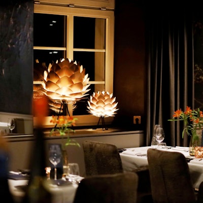 Eingedeckter Tisch mit Blumen, stimmungsvoll beleuchtet von artischockenförmigen Pendelleuchten.