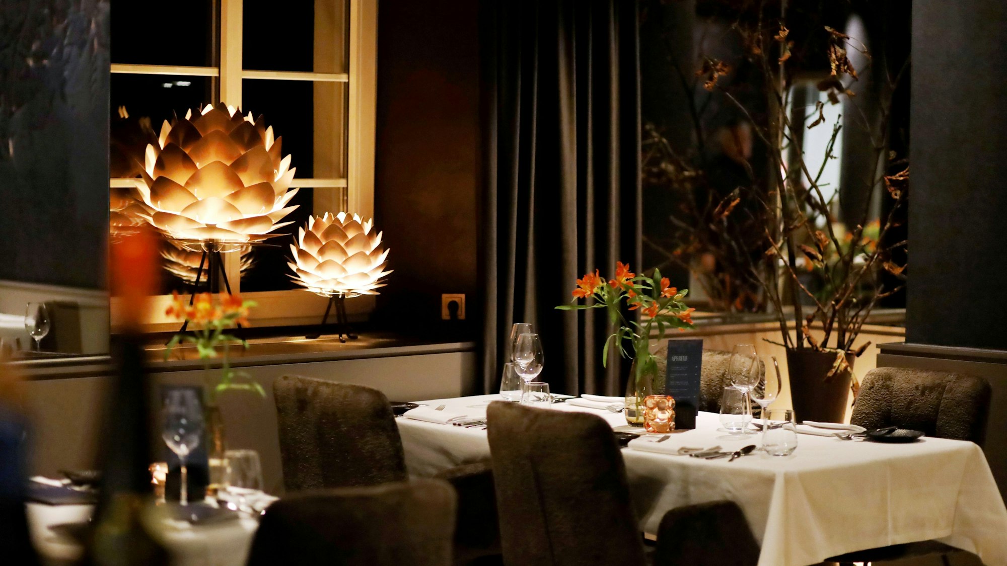 Eingedeckter Tisch mit Blumen, stimmungsvoll beleuchtet von artischockenförmigen Pendelleuchten.