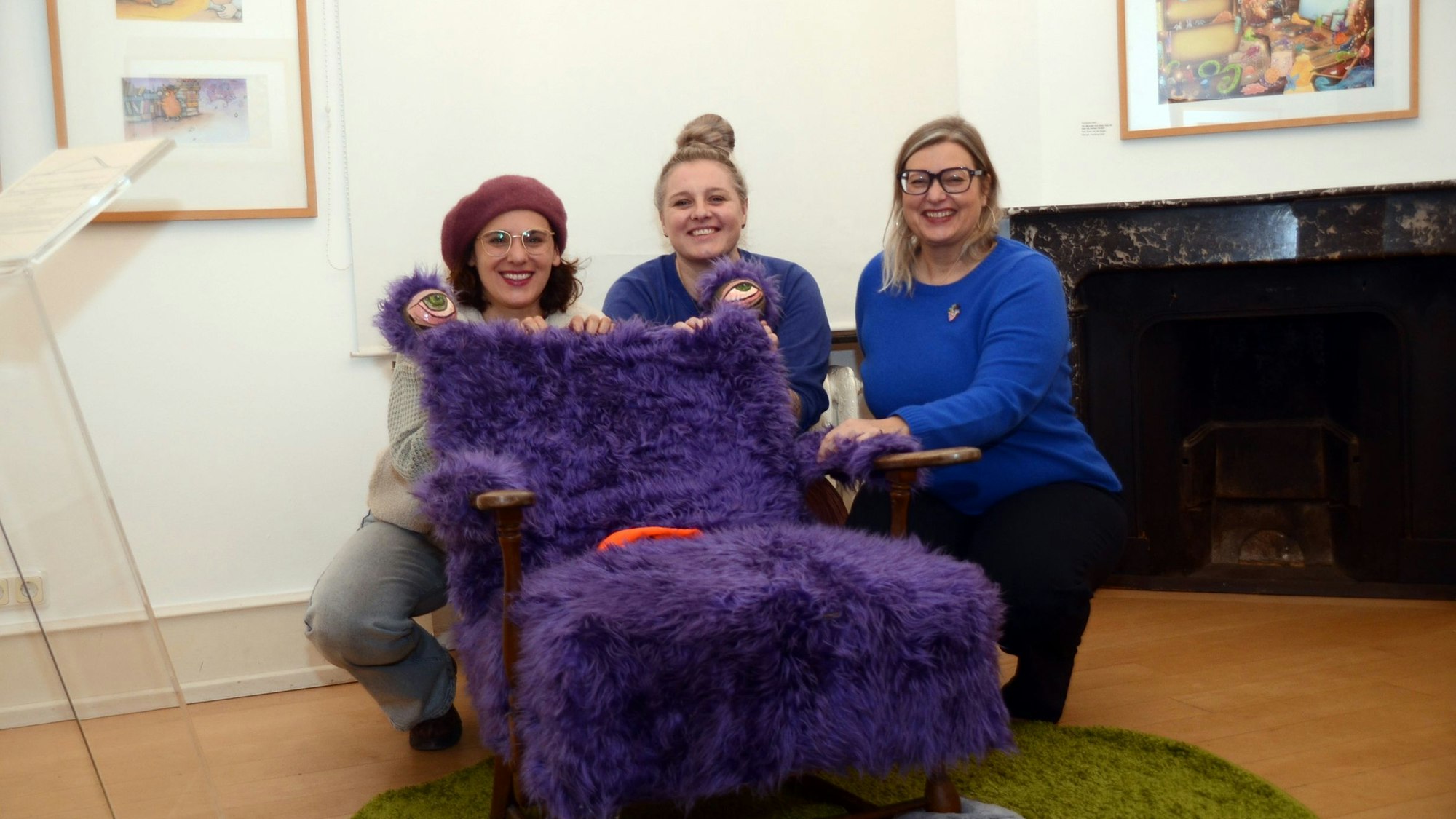 Drei Frauen hocken hinter einem mit lila Kunstfell bezogenen Sessel.