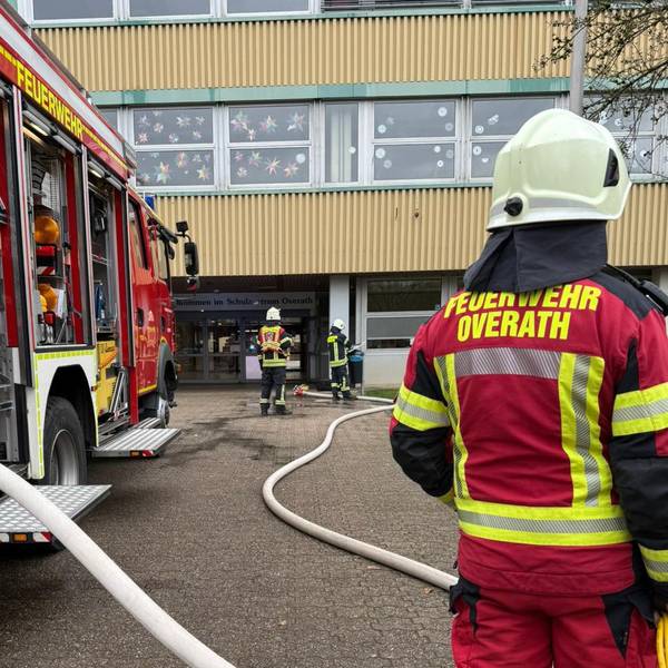 Feuerwehrleute stehen mit einem Löschfahrzeug vor dem Overather Schulzentrum Cyriax.