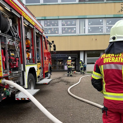 Feuerwehrleute stehen mit einem Löschfahrzeug vor dem Overather Schulzentrum Cyriax.