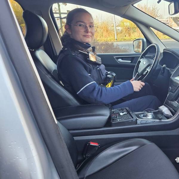 Zu sehen ist eine Polizistin am Steuer eines Streifenwagens.
