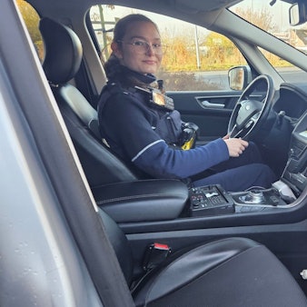 Zu sehen ist eine Polizistin am Steuer eines Streifenwagens.