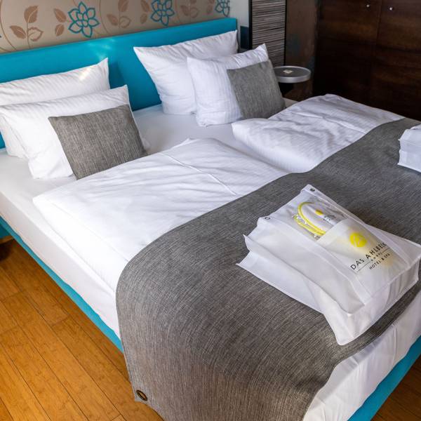 Das Bild zeigt ein Doppelbett in einem Hotel, auf dem zwei Taschen liegen.