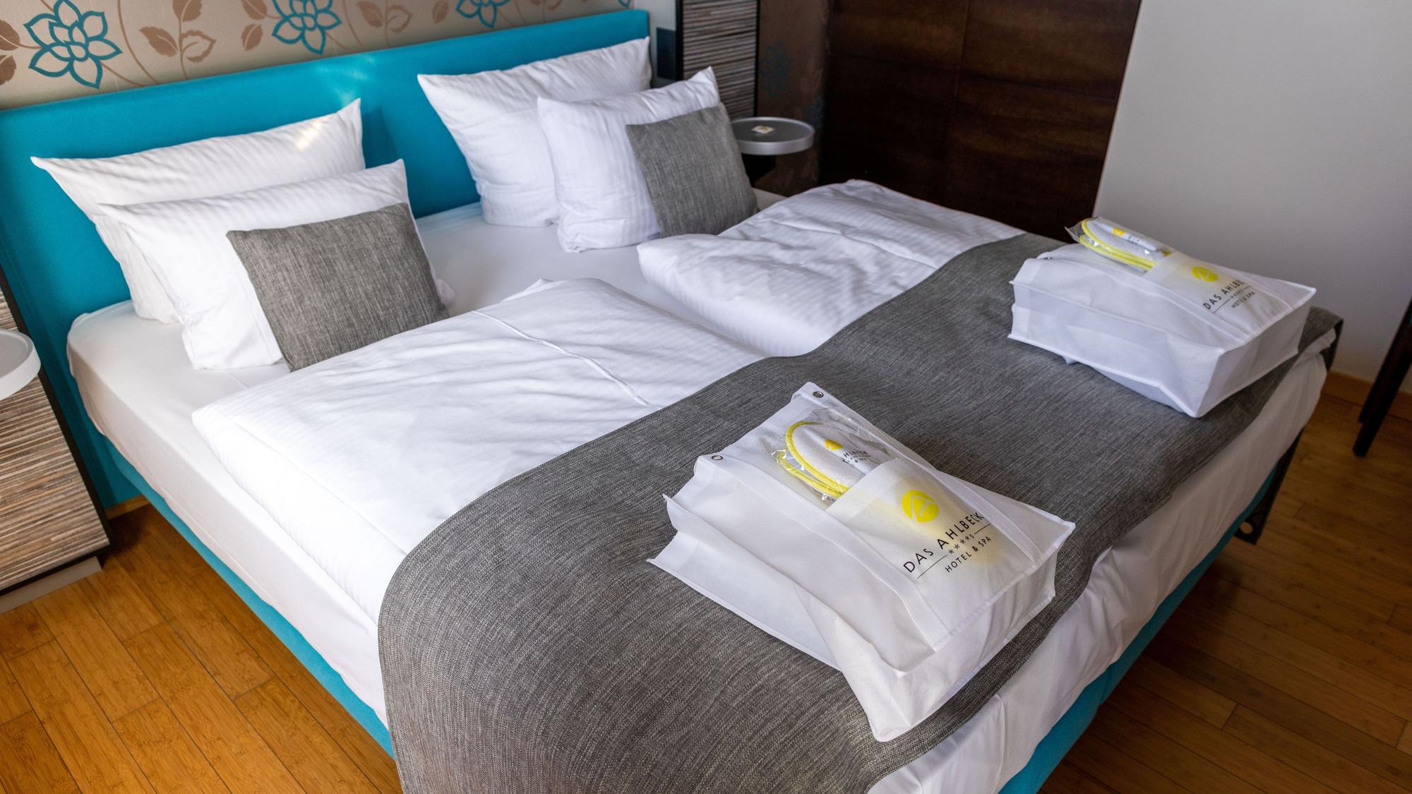 Das Bild zeigt ein Doppelbett in einem Hotel, auf dem zwei Taschen liegen.