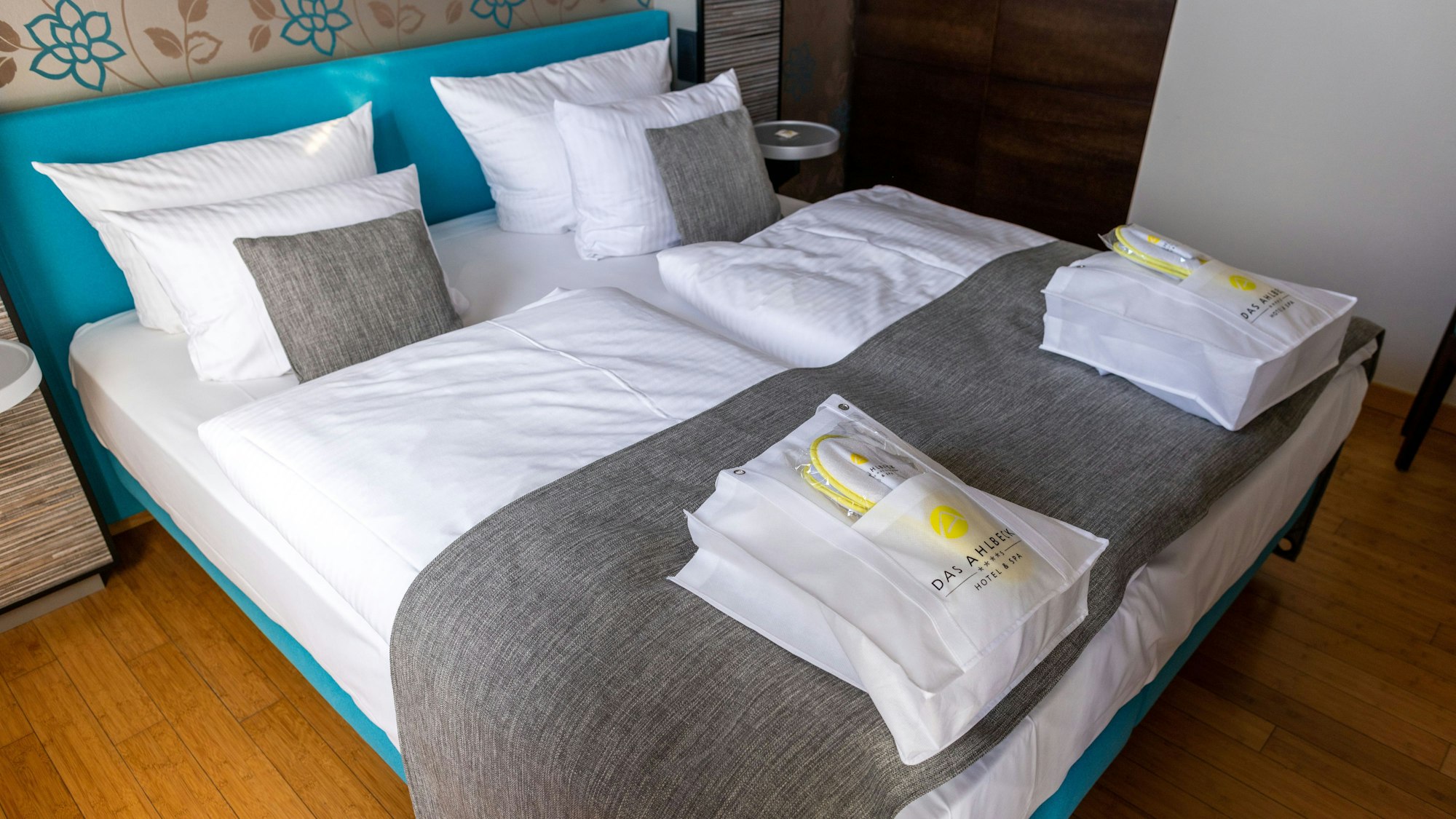 Das Bild zeigt ein Doppelbett in einem Hotel, auf dem zwei Taschen liegen.