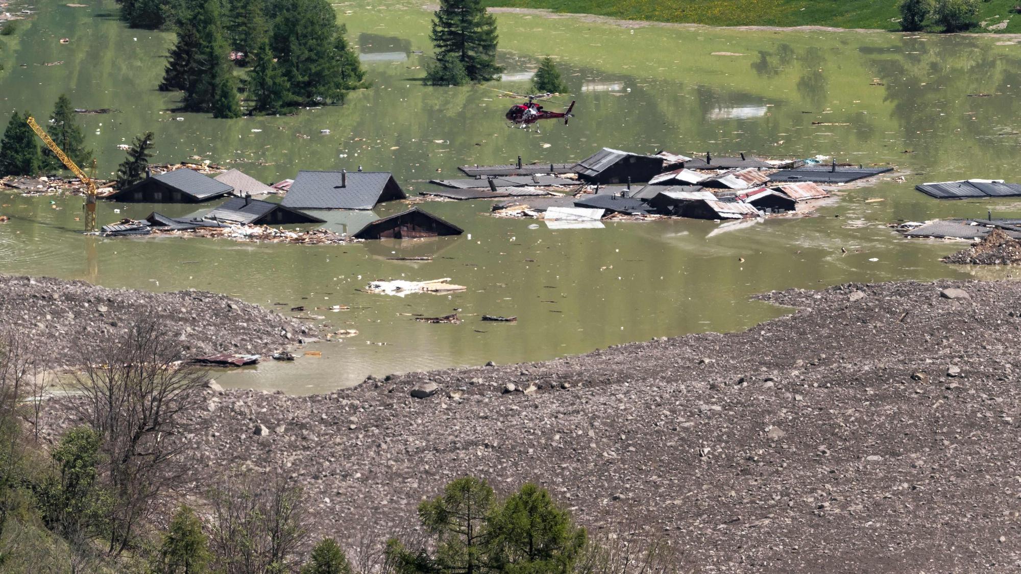 Ein Helikopter fliegt über die Trümmer und zerstörten Häuser von Blatten, die in den aufgestauten Wassermassen der Lonza liegen. Nach dem Kollaps des Birchgletschers am 28. Mai 2025 hatte ein massiver Bergsturz tonnenweise Fels, Eis und Geröll ins Tal geschleudert und das zuvor evakuierte Dorf zerstört.