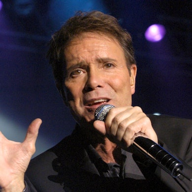 Cliff Richard singt in ein Mikrofon.