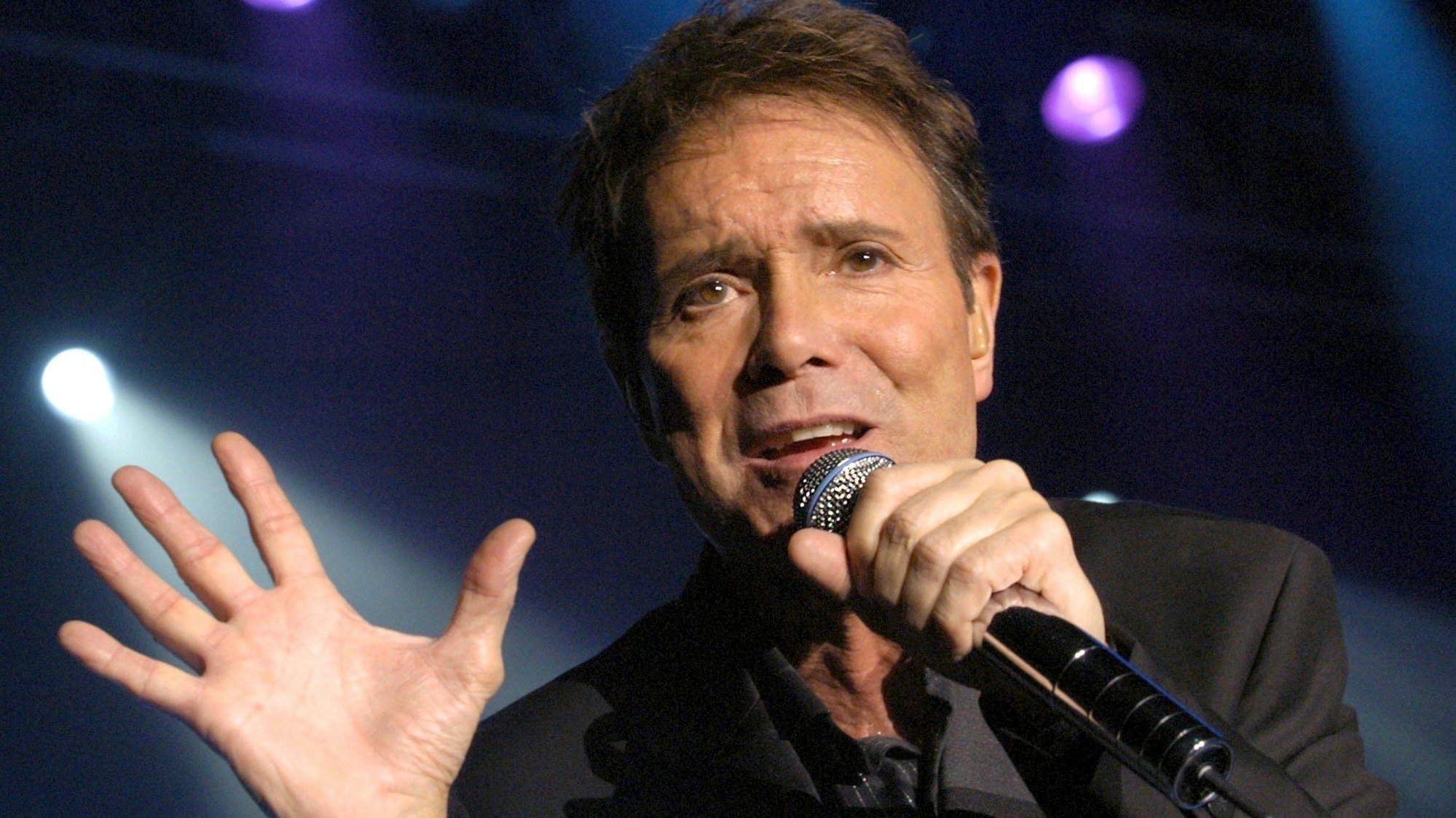 Cliff Richard singt in ein Mikrofon.