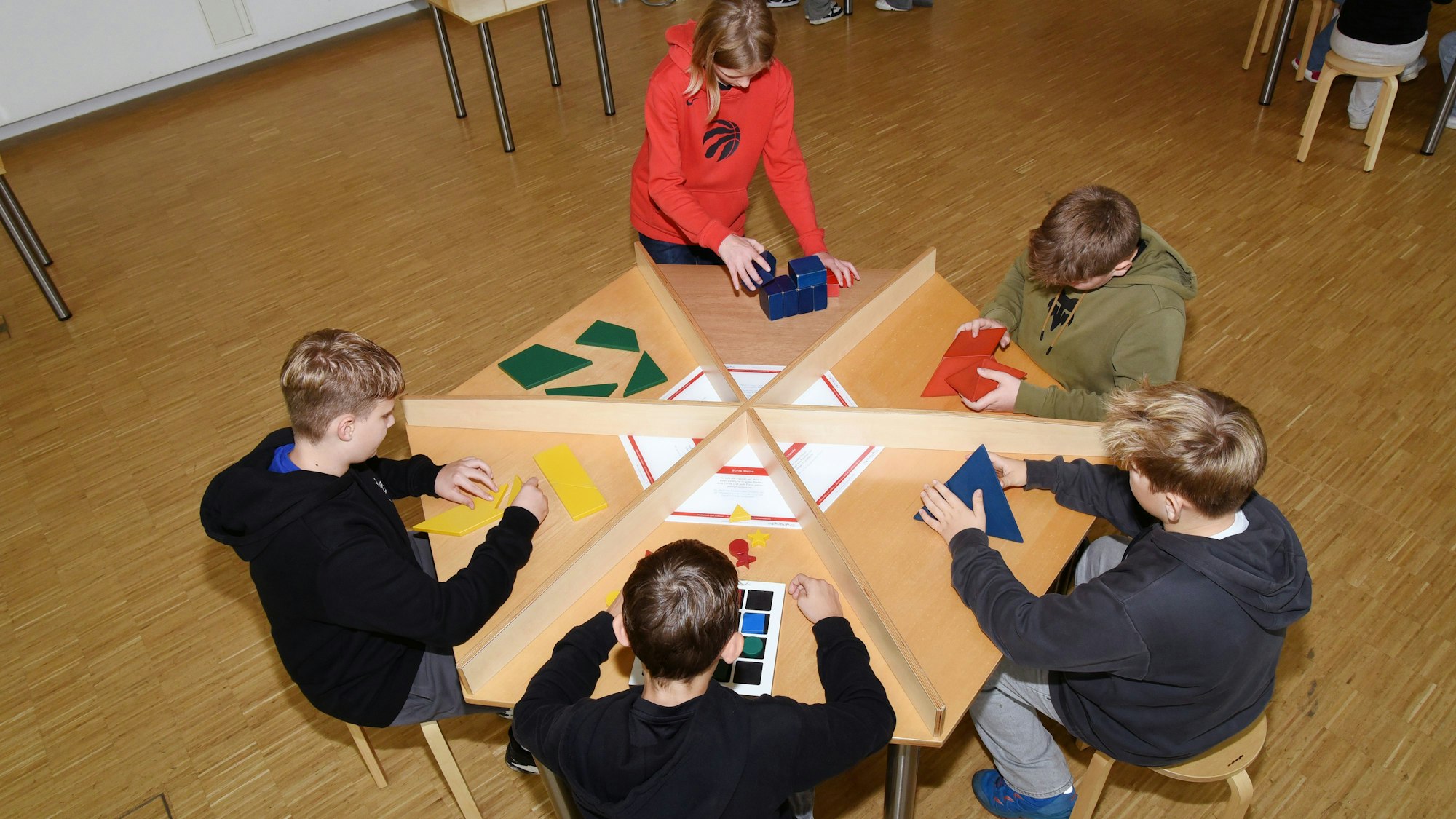 Kinder sitzen an einem Tisch im Kreis und knobeln.