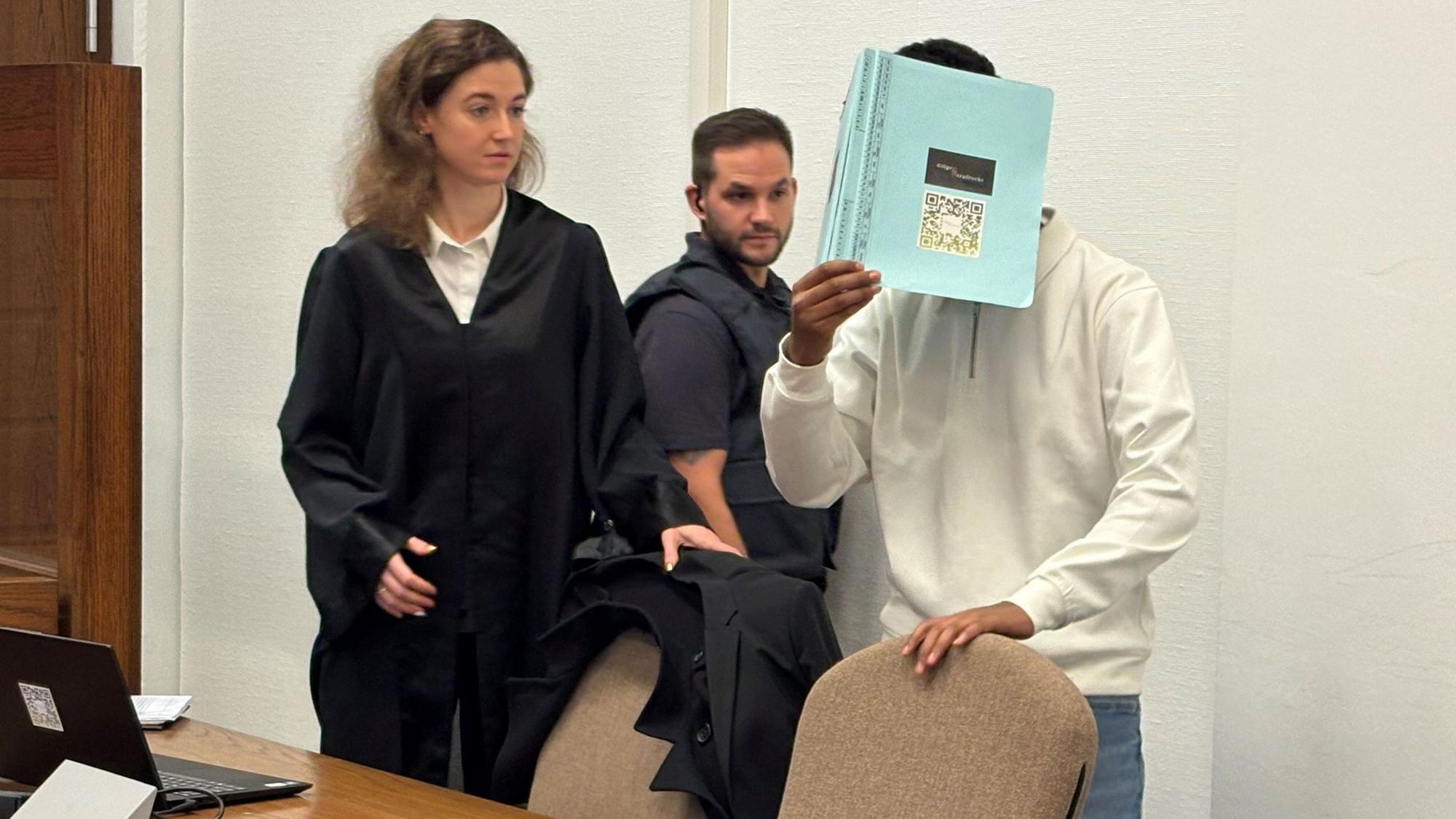 Der angeklagte 18-Jährige wird von einem Wachtmeister in den Gerichtssaal gebracht. Links seine Verteidigerin.