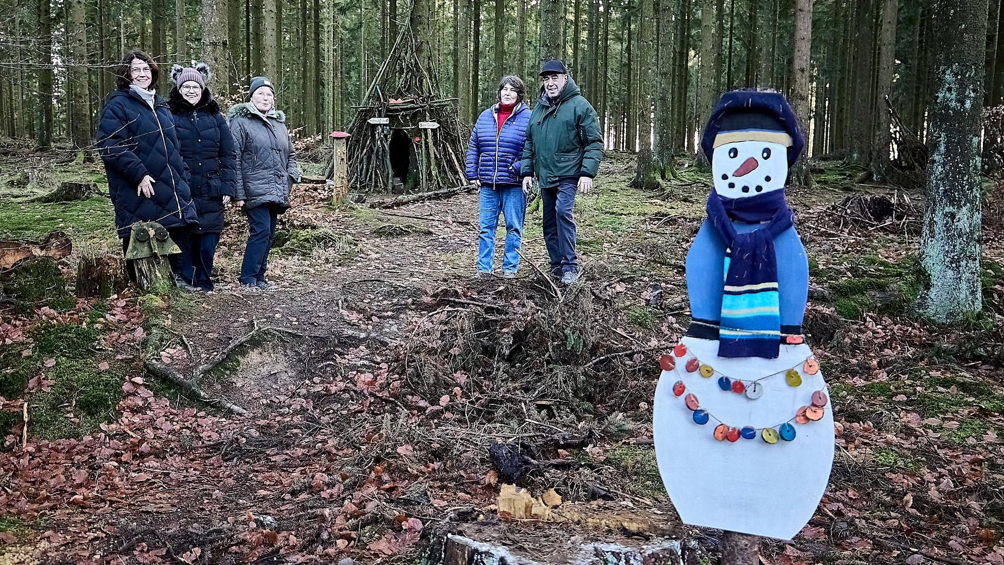 Mitten im Wald stehen die Personen, die den Krippenweg vorgestellt haben. Im Hintergrund sieht man die Schutzhütte, im Vordergrund einen selbstgebastelten Papp-Schneemann mit Schal.