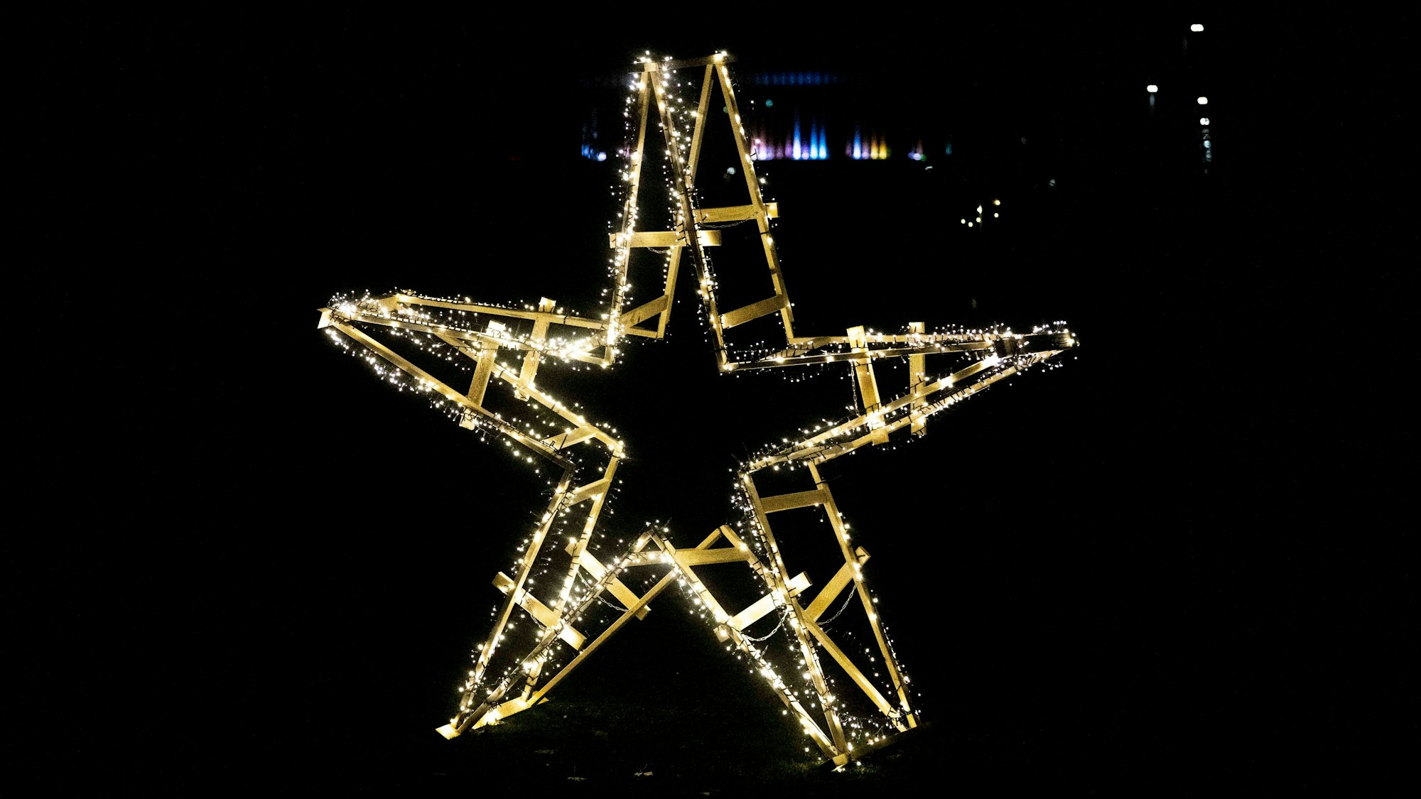 Das Bild zeigt einen aus Holzböcken zusammengebauten Holzstern samt leuchtender Lichterkette in der Dunkelheit.