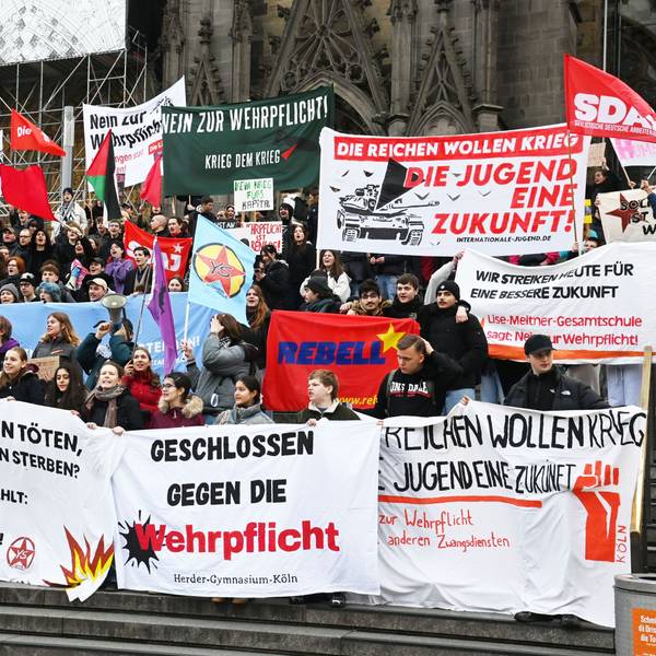 Vor den Treppen zum Dom halten verschiedene Jugendorganisationen und -gruppen Banner hoch, um gegen den Wehrdienst zu demonstrieren.