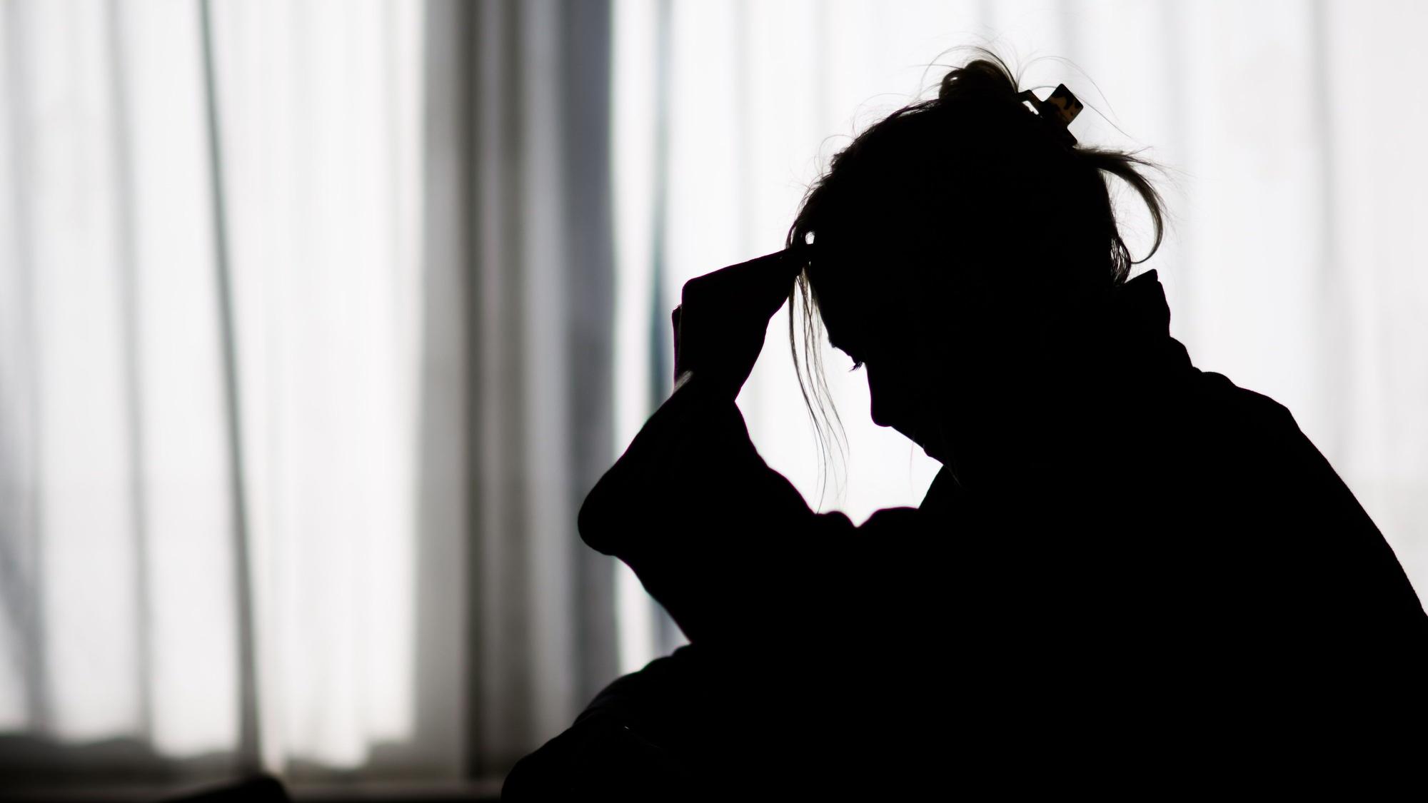 Die Silhouette einer Frau zeichnet sich vor einer hellen Fensterfront ab (gestellte Szene).