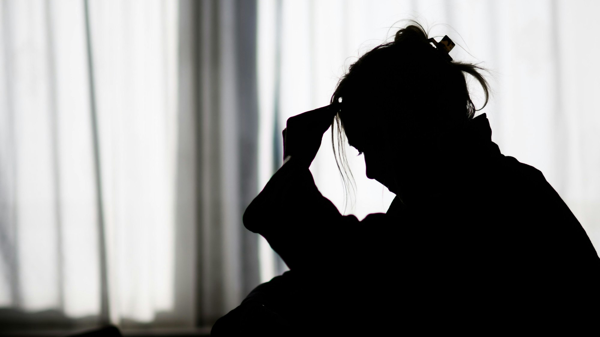 Die Silhouette einer Frau zeichnet sich vor einer hellen Fensterfront ab (gestellte Szene).