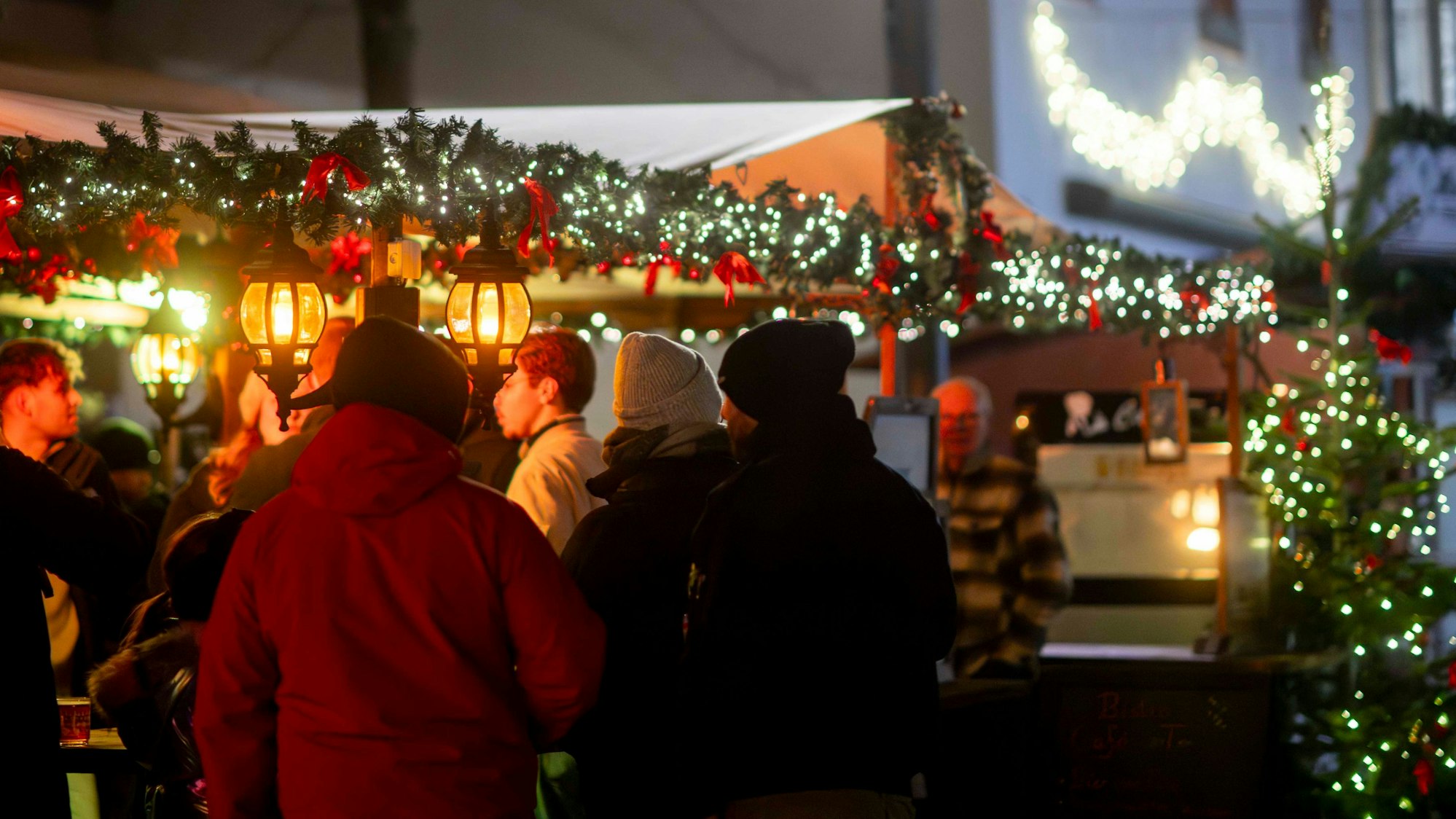 In der Dämmerung stehen Menschen an einer stimmungsvoll beleuchteten Bude auf dem Weihnachtsmarkt in Bad Münstereifel.