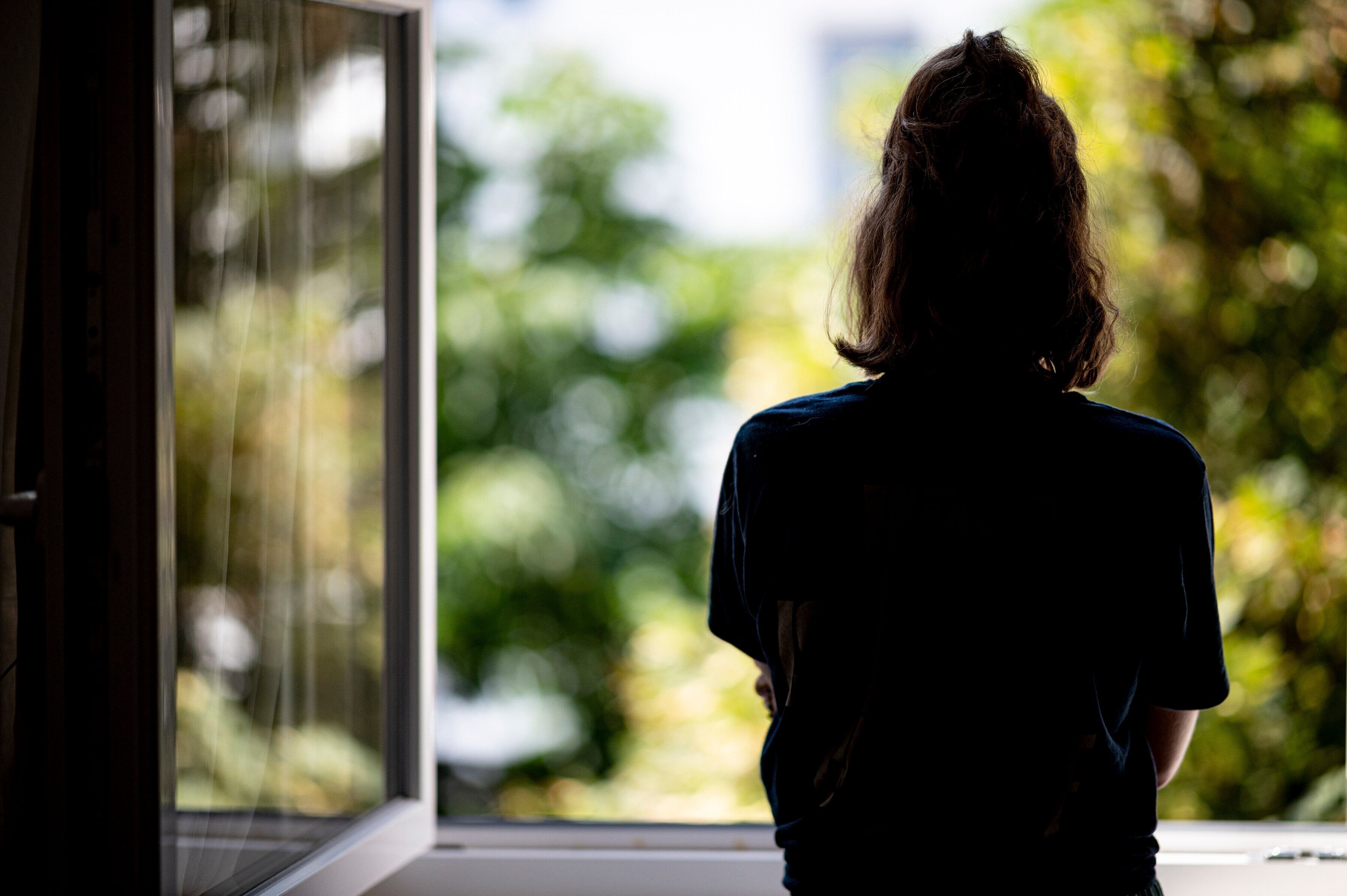 ILLUSTRATION - Eine Frau steht in ihrer Wohnung an einem Fenster.