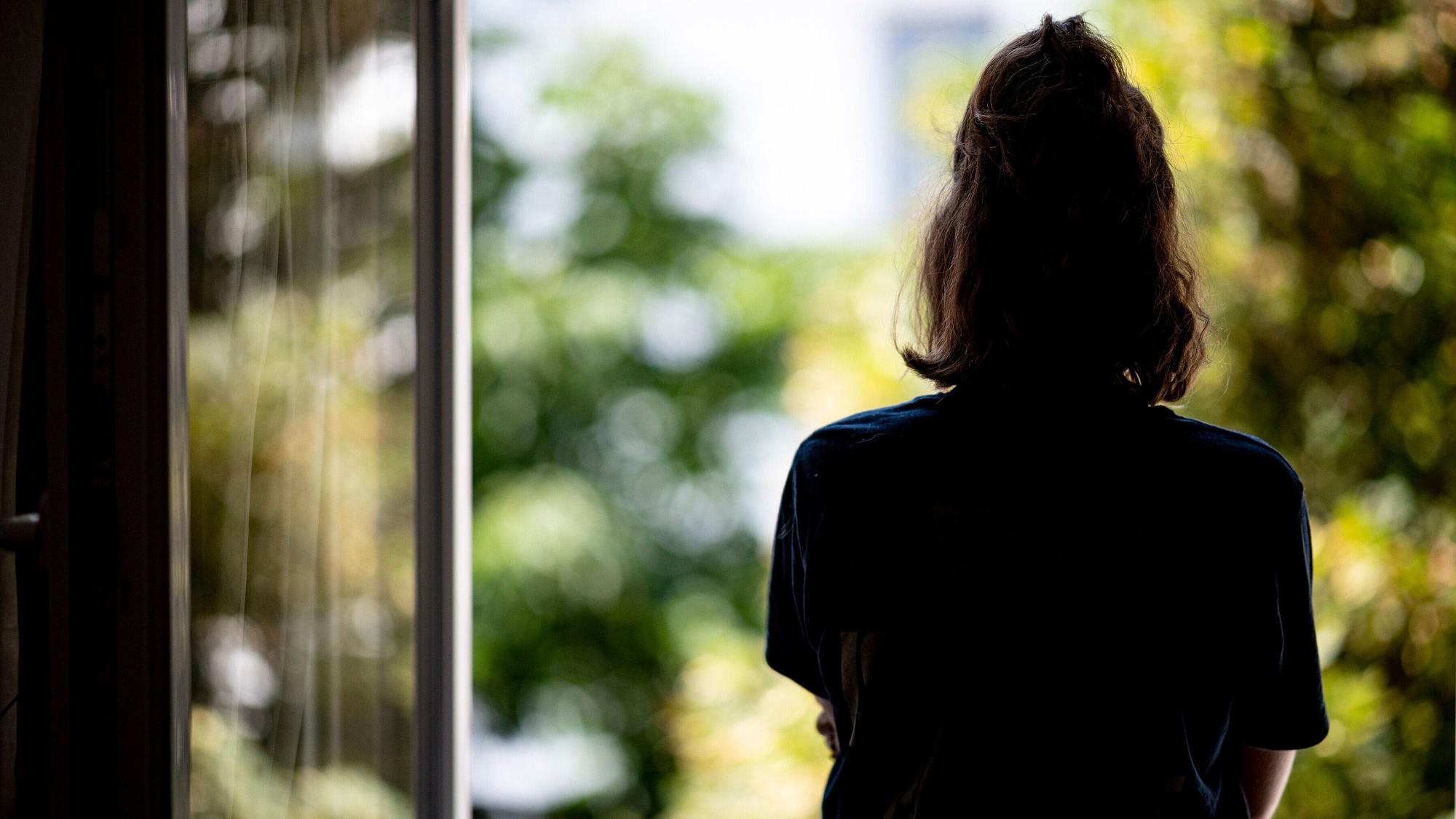 ILLUSTRATION - Eine Frau steht in ihrer Wohnung an einem Fenster.