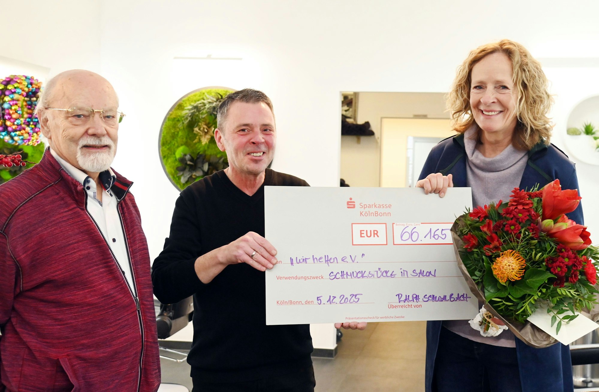 Goldschmiedemeister Herbert Schmelzer und Friseurmeister Ralph Schwalbach überreichen Isabella Neven DuMont für „wir helfen“ einen symbolischen Scheck.