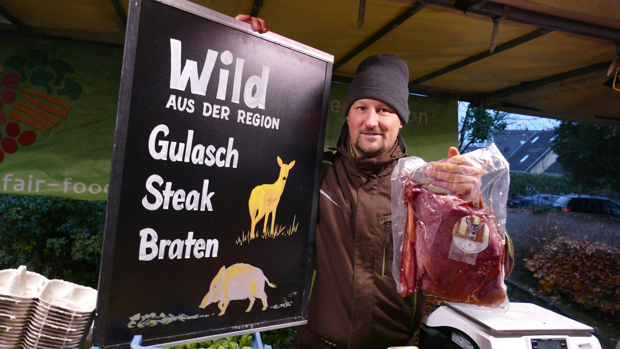 Ein Mann an einem Marktstand vor einem Schild mit der Aufschrift "Wild aus der Region"