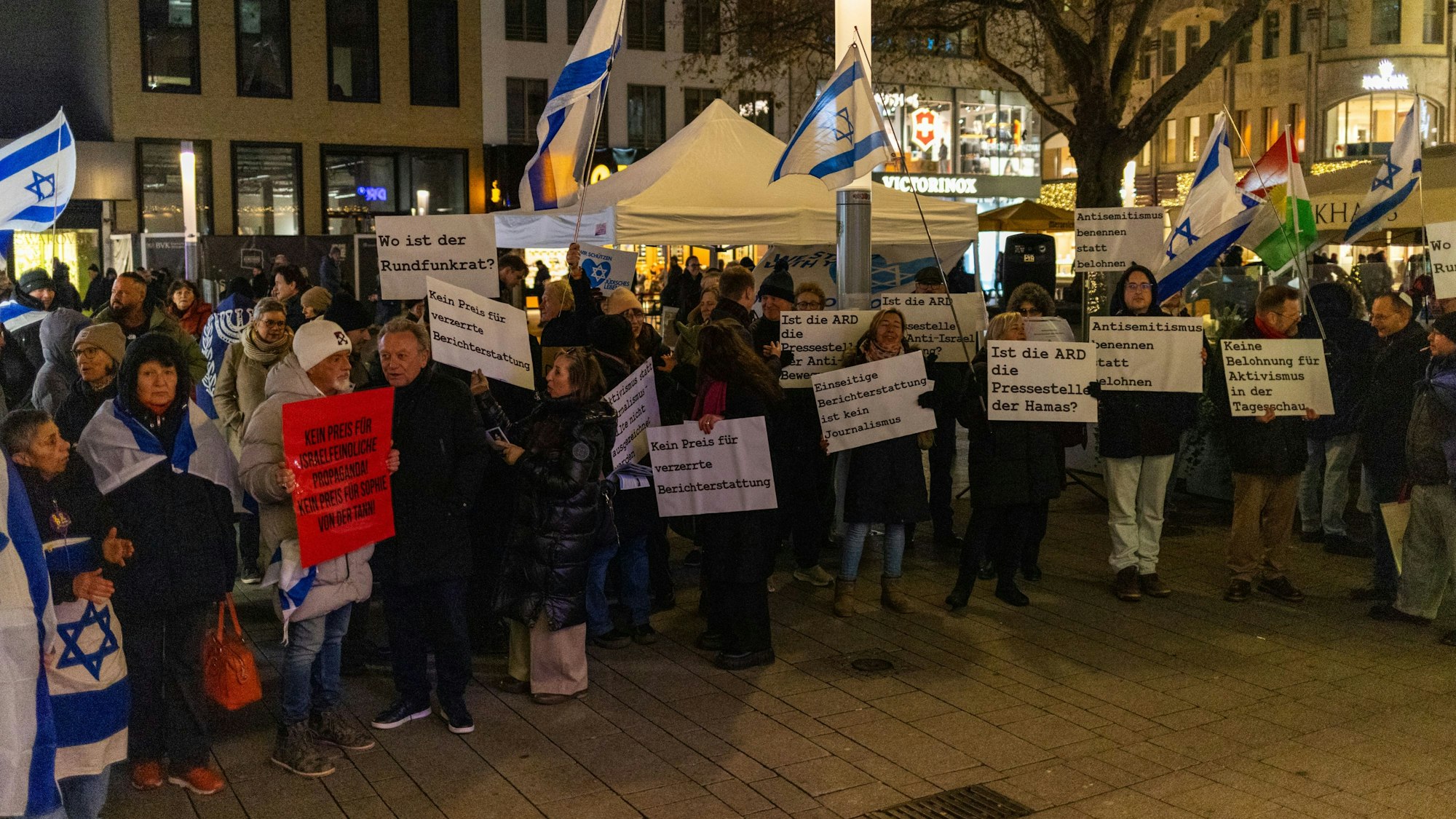 Menschen stehen an einem Platz. Sie zeigen Plakate und wehen Israel-Fahnen.