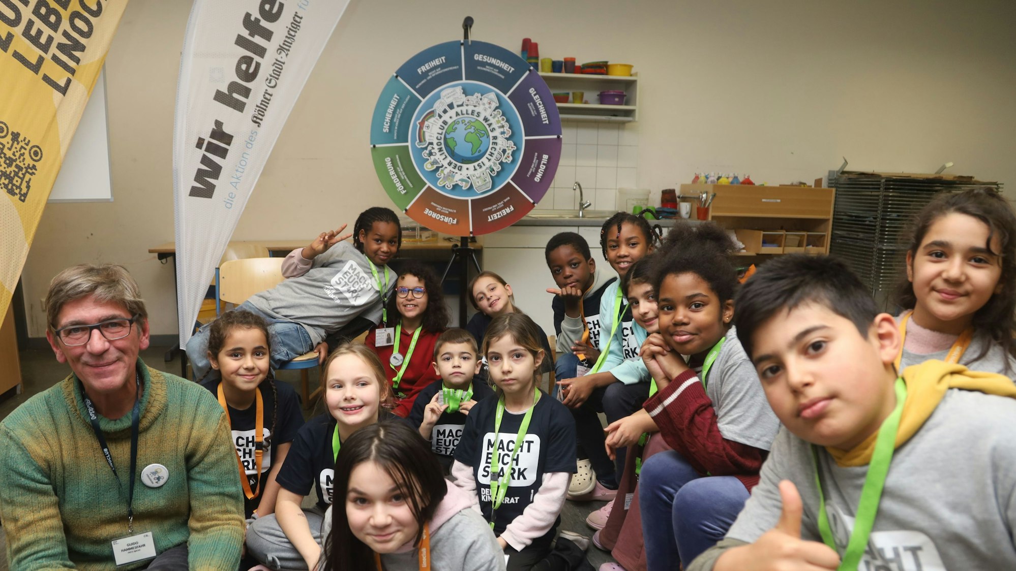 14 Jungen und Mädchen des Linoclub-Kinderrats sitzen in einer Gruppe um Löwenzahn-Hauptdarsteller Guido Hammesfahr alias Fritz Fuchs. Sie tragen T-Shirts mit der Aufschrift „Macht euch stark!“