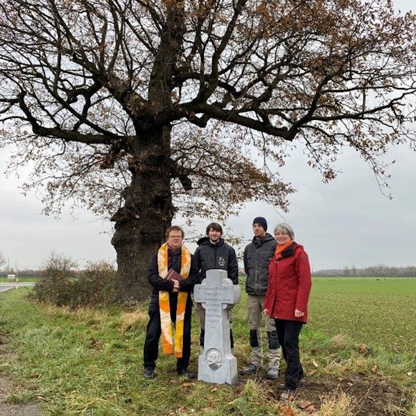 Das Foto zeigt Menschen, die vor einem Baum an einem Kreuzchen stehen.