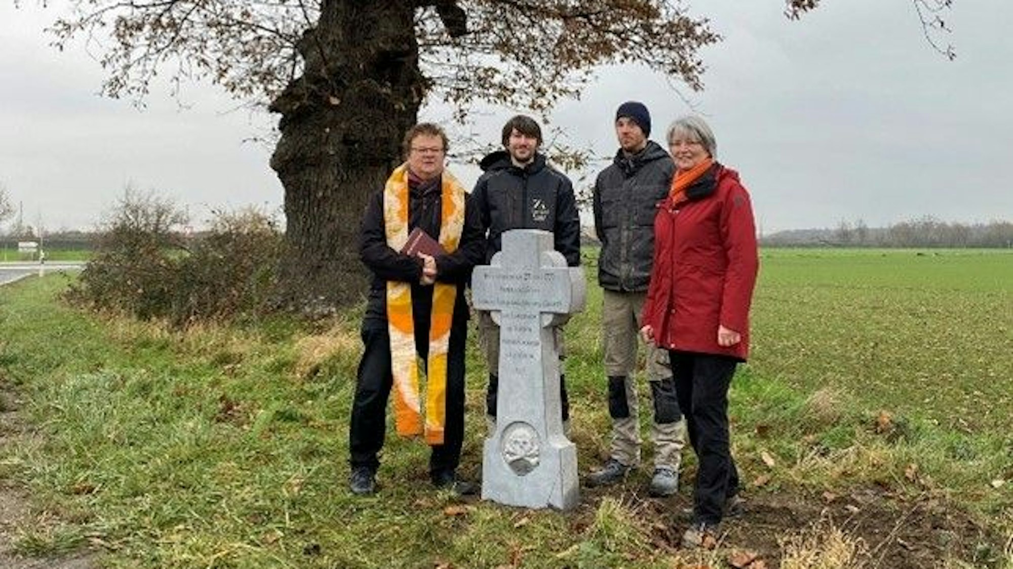 Das Foto zeigt Menschen, die vor einem Baum an einem Kreuzchen stehen.
