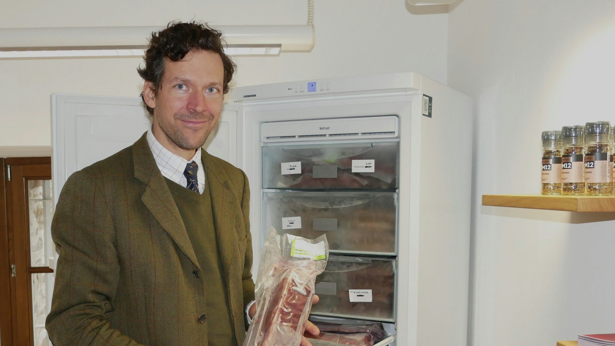 Ein Mann im Anzug vor einem Tiefkühlschrank. Er hält ein Stück Fleisch in der Hand.