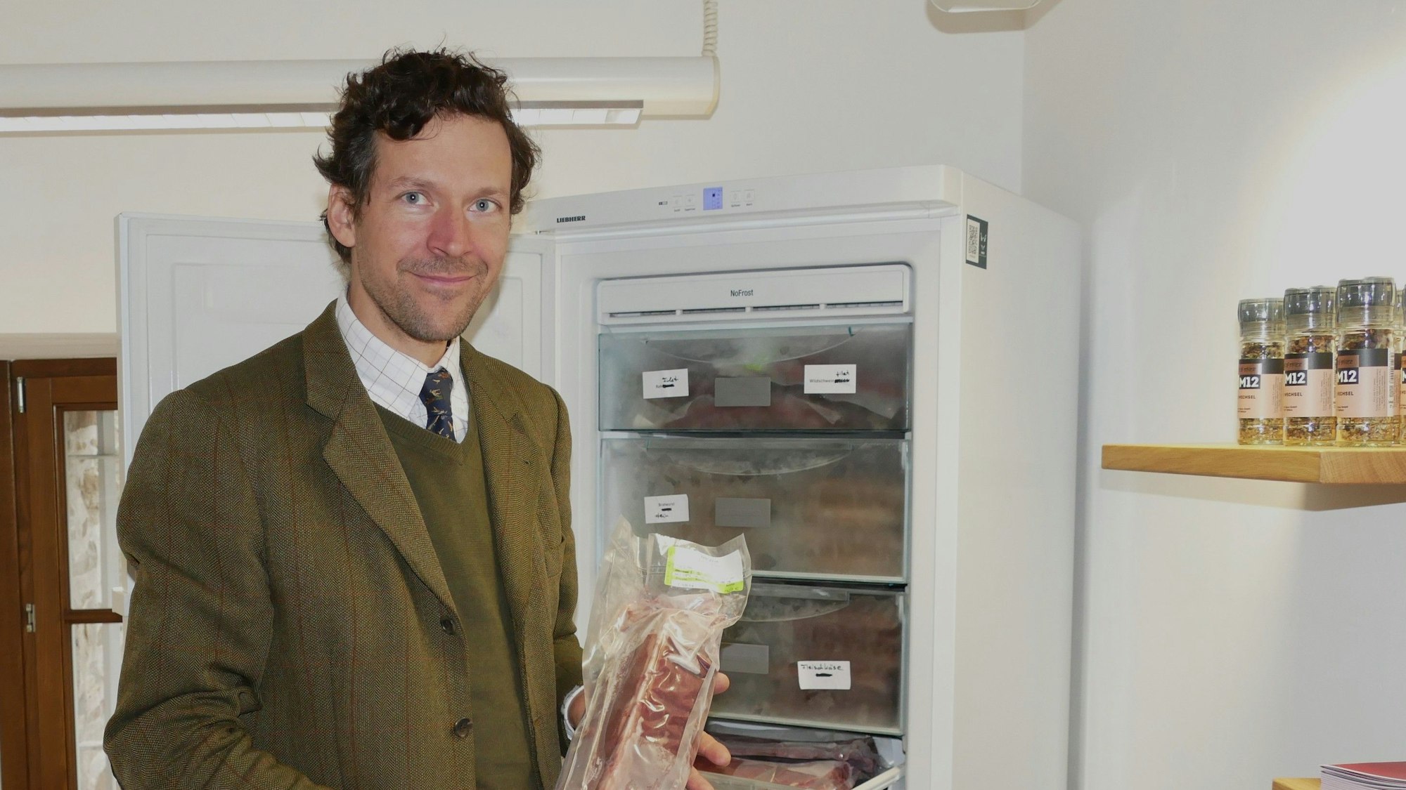 Ein Mann im Anzug vor einem Tiefkühlschrank. Er hält ein Stück Fleisch in der Hand.