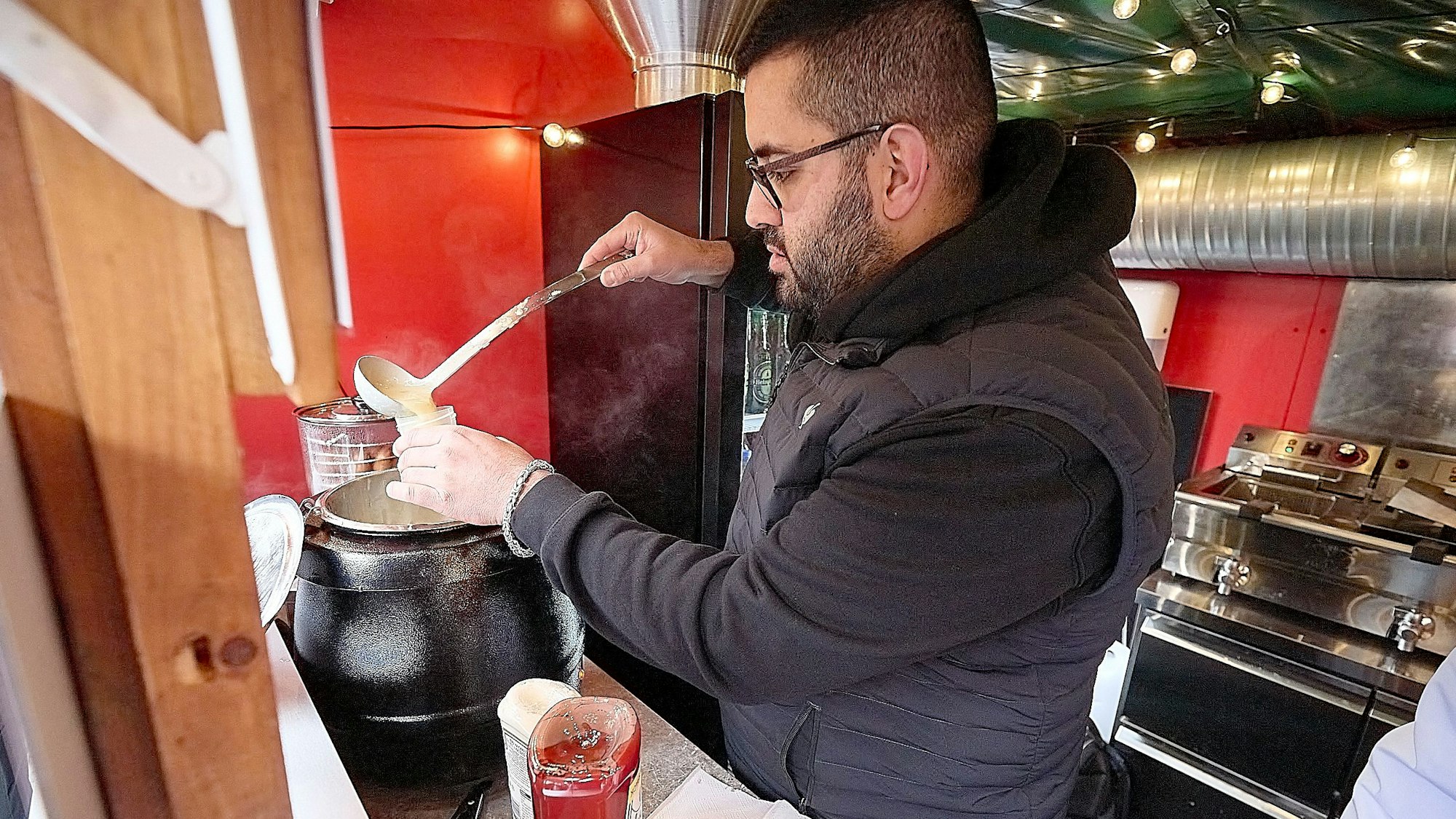 Abbas Kteich steht in einer Imbissbude auf dem Weihnachtsmarkt in Monschau. Er füllt Suppe in ein kleines Gefäß, die später im Labor untersucht wird.