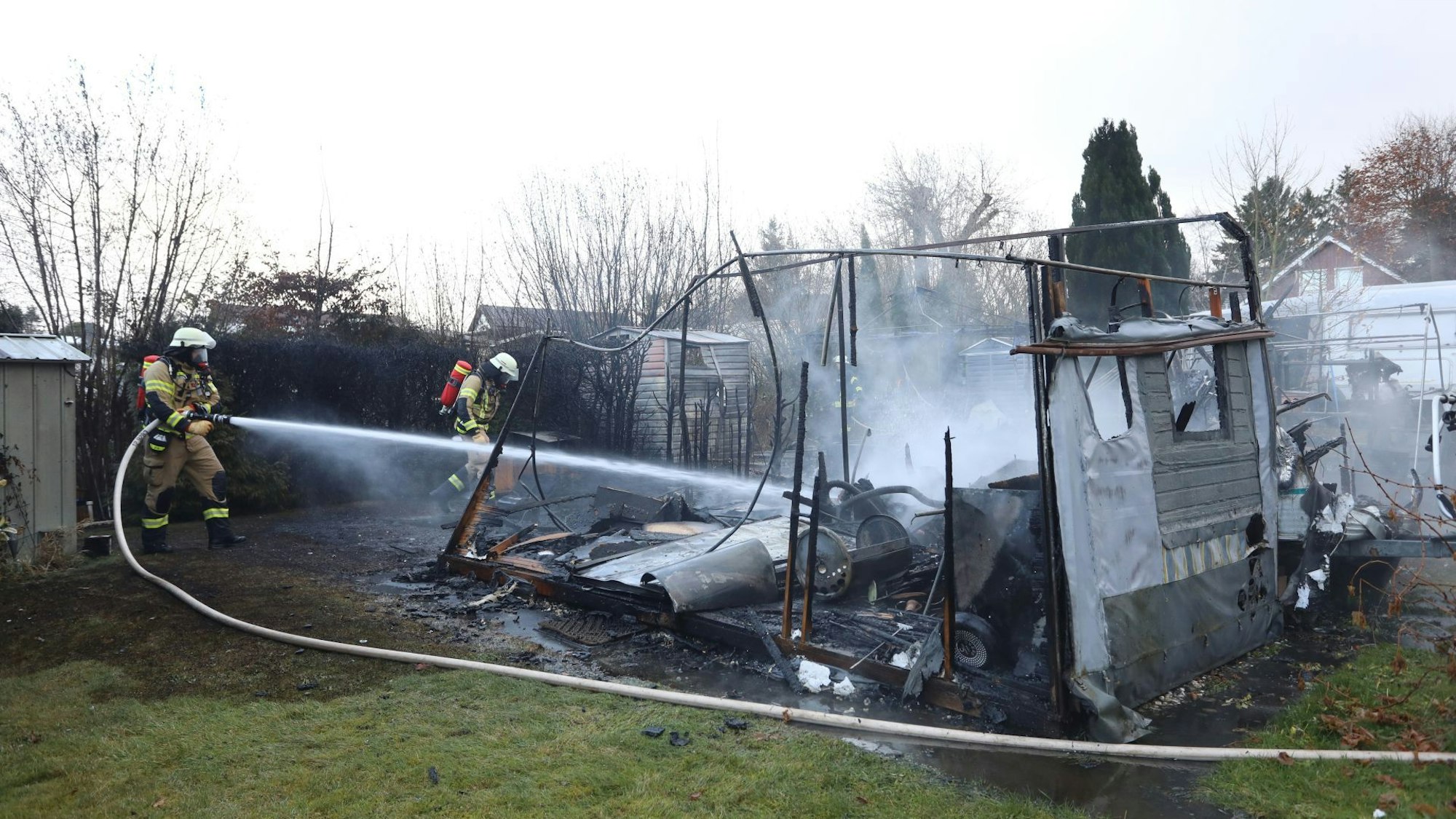Zwei Feuerwehrleute löschen die verkohlten Reste von zwei Wohnwagen.