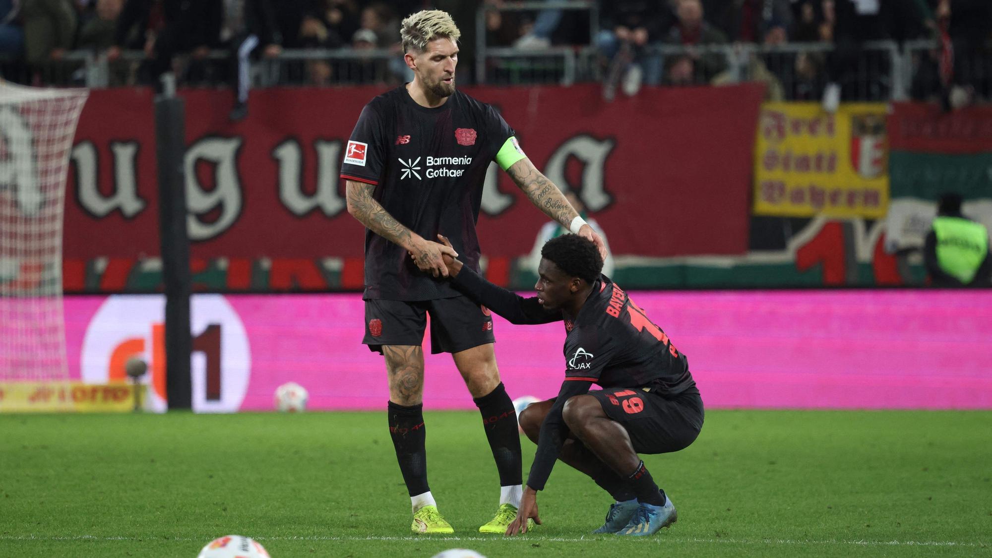 Bayer Leverkusen's German midfielder #08 Robert Andrich (L) helps up deceived Bayer Leverkusen's Dutch forward #19 Ernest Poku after the end of the German first division Bundesliga football match between FC Augsburg and Bayer Leverkusen in Augsburg, southern Germany, on December 6, 2025. (Photo by Karl-Josef HILDENBRAND / AFP) / DFL REGULATIONS PROHIBIT ANY USE OF PHOTOGRAPHS AS IMAGE SEQUENCES AND/OR QUASI-VIDEO
