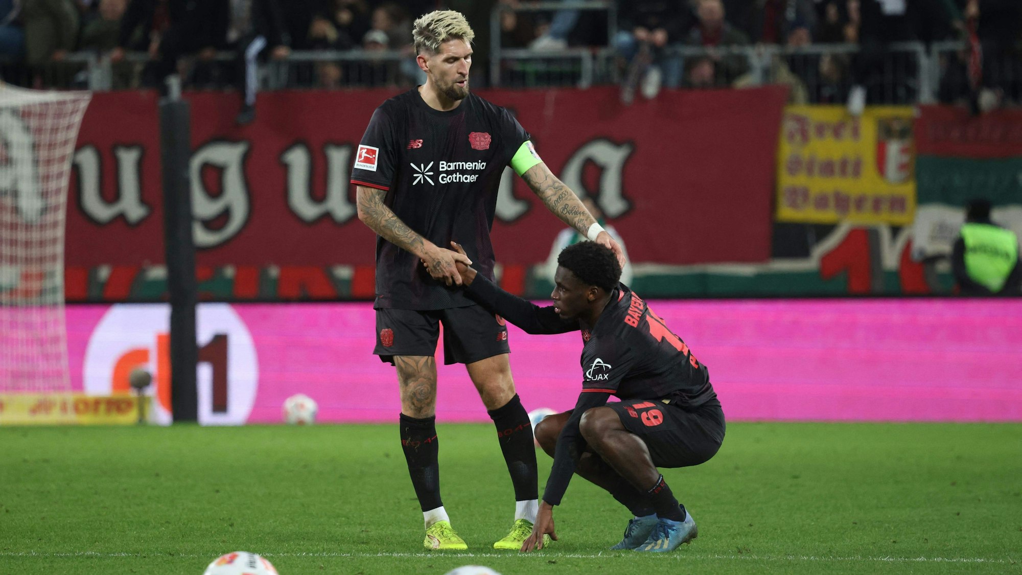 Bayer Leverkusen's German midfielder #08 Robert Andrich (L) helps up deceived Bayer Leverkusen's Dutch forward #19 Ernest Poku after the end of the German first division Bundesliga football match between FC Augsburg and Bayer Leverkusen in Augsburg, southern Germany, on December 6, 2025. (Photo by Karl-Josef HILDENBRAND / AFP) / DFL REGULATIONS PROHIBIT ANY USE OF PHOTOGRAPHS AS IMAGE SEQUENCES AND/OR QUASI-VIDEO