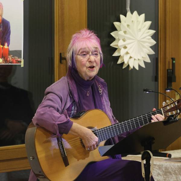 Monika Kampmann sitz mit ihrer Gitarre vor einem Notenständer und singt.