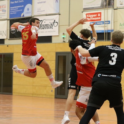 Palmersheims Spieler Nils Schouren steigt zum Wurf hoch. Ein Gegner vor ihm reißt die Arme hoch. Hinter ihm befinden sich ein Mitspieler und ein weiterer Gegenspieler.