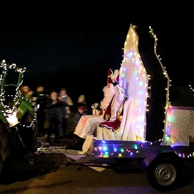 Ein mit Lichterketten geschmückter Trecker zieht einen Anhänger, auf dem der Nikolaus sitzt.