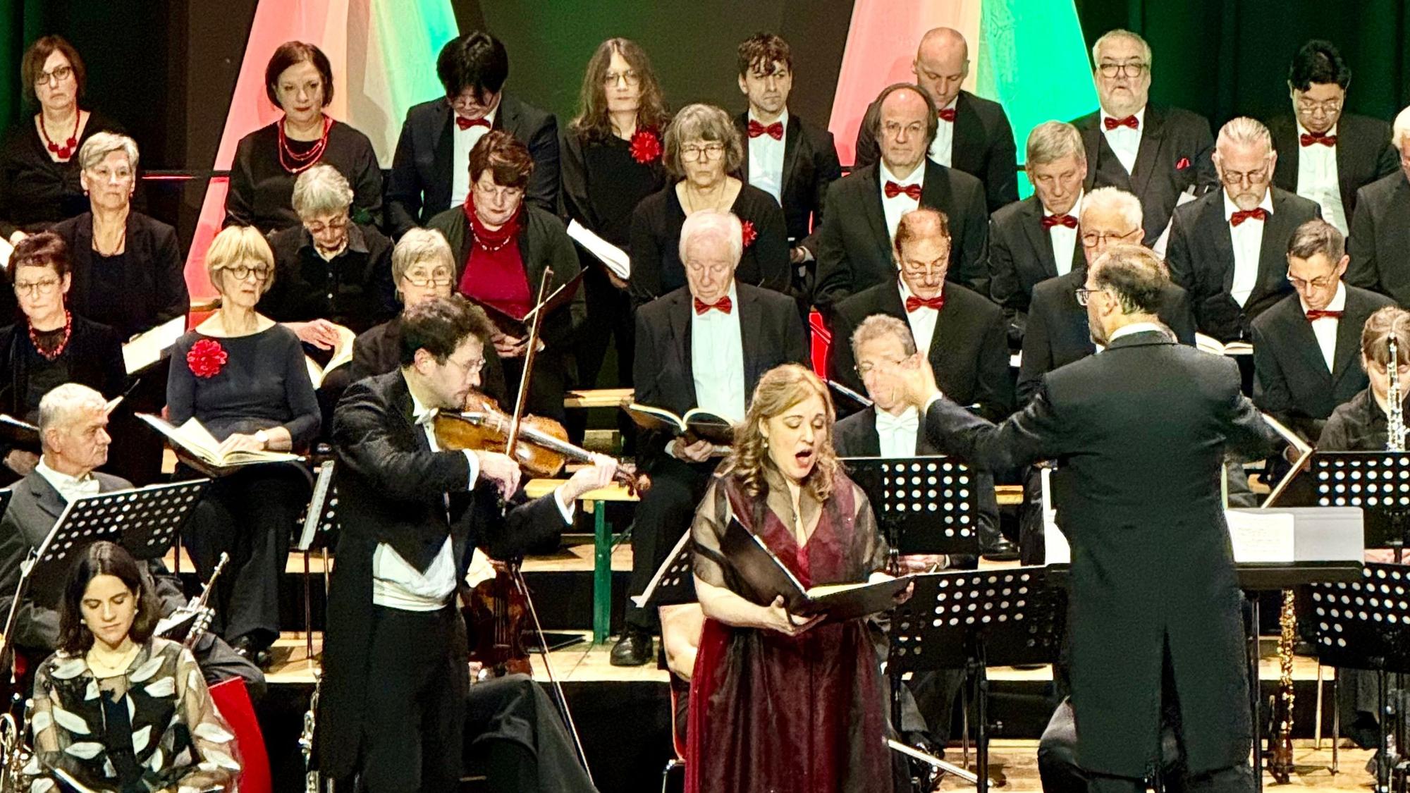 Ein Chor im Hintergrund, davor das Orchester, im Vordergrund eine Sängerin.