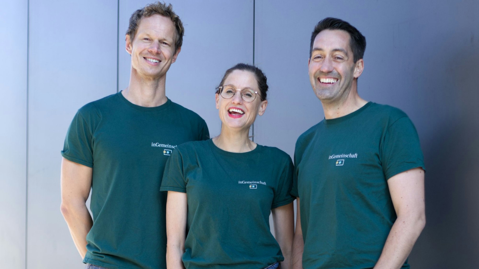 Zwei Männer und eine Frau in blauen Shirts lächeln in die Kamera