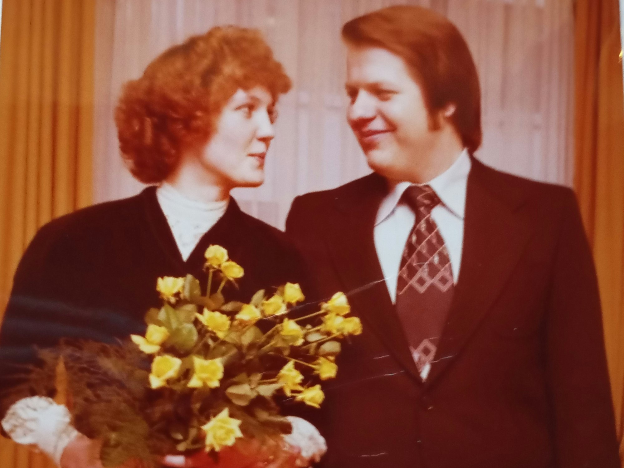 Ein lächelndes Brautpaar. Sie hält einen Blumenstrauß in den Händ.en.