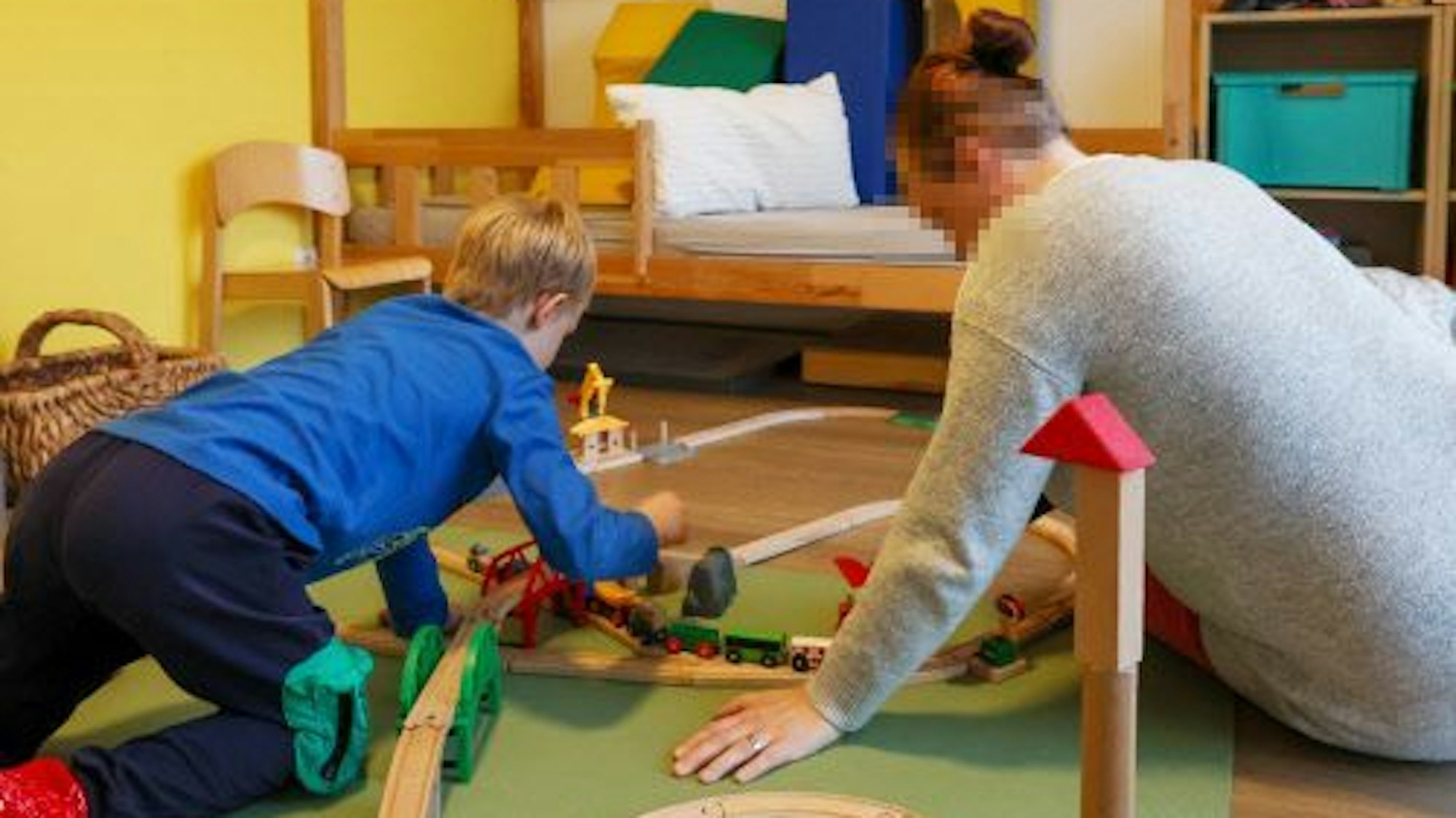 Eine Frau spielt auf dem Boden mit ihrem Sohn mit einer Eisenbahn.