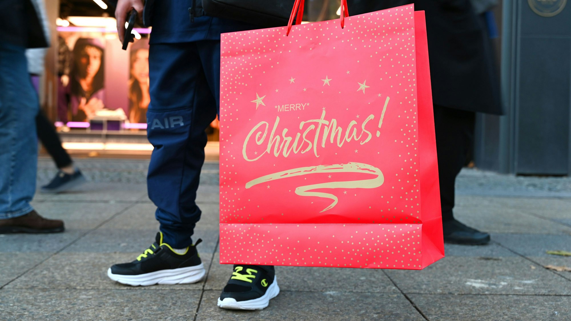 Ein Mann steht mit einer weihnachtlichen Verkaufstüte mit dem Spruch «Merry Christmas» auf einer Einkaufsstraße.